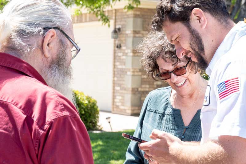 A uniformed service technician showing his phone to a homeowner couple outside their home